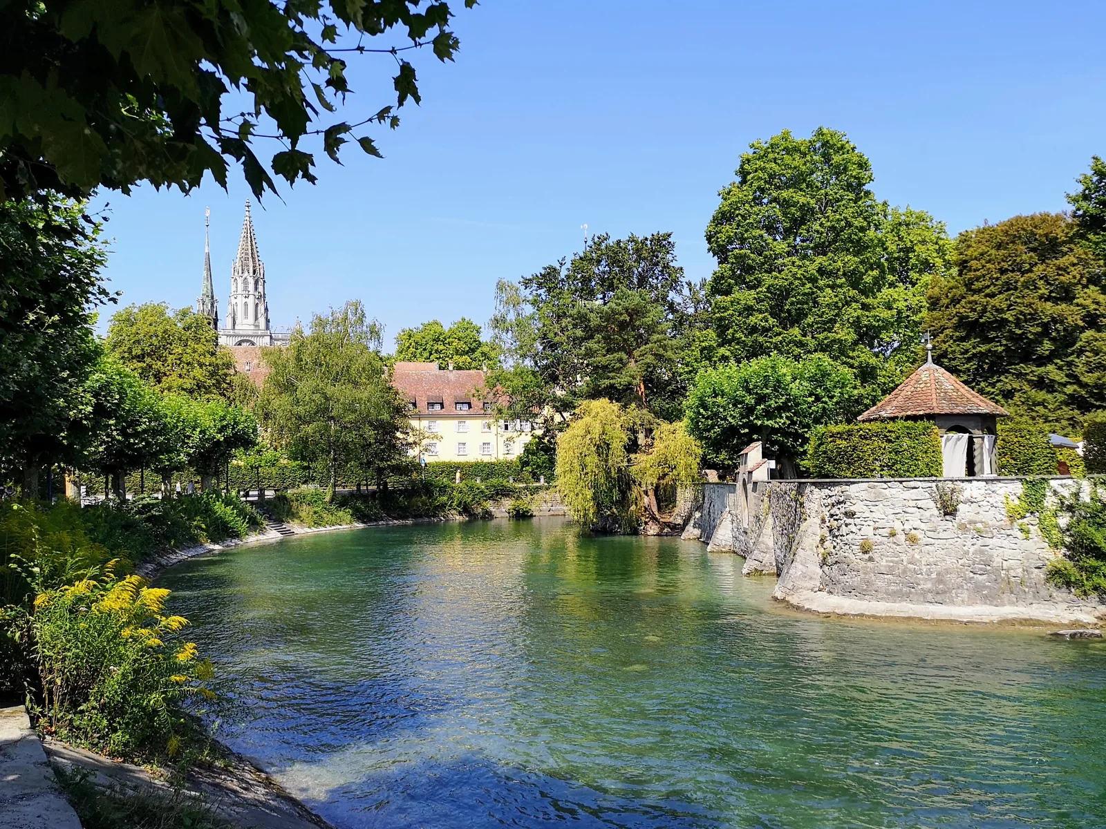 Grünes Ufer mit Stadtmauer in Konstanz, im Hintergrund der Münsterturm